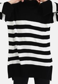 Pull à rayures noires et blanches avec un col montant, des manches larges et une coupe ample. Il présente une texture côtelée et des fentes latérales à l'ourlet.