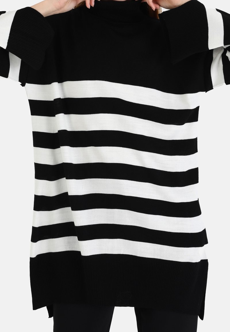 Pull à rayures noires et blanches avec un col montant, des manches larges et une coupe ample. Il présente une texture côtelée et des fentes latérales à l'ourlet.