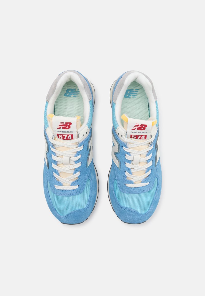 Blaue Sneakers aus Wildleder und Mesh-Material mit weißen Akzenten, grauem Absatz und einem roten Etikett mit der Aufschrift "New Balance 574."