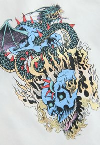 Modrý drak s červenými hroty chrlící plamen kolem hořící modré lebky s ostrými zuby a tmavými očními důlky na bílém pozadí.