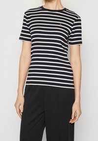 Navy ja valge triibuline T-särk, mis on valmistatud pehmest kangast, ümarate kaeluste ja lühikeste varrukatega, rinnas on väike logo.