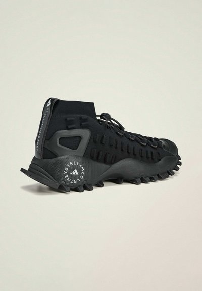 Scarpa sportiva nera con parte superiore in maglia flessibile, suola in gomma testurizzata e un design del tallone distintivo con accenti del logo.