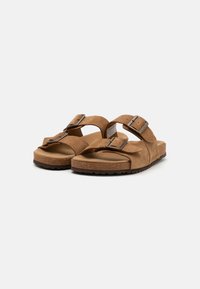 Sandalias de ante marrón con dos correas ajustables y hebillas de metal, con una plantilla de corcho texturizado y una suela de goma texturizada.