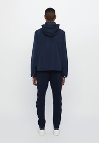 Marineblå hettegenser med lange ermer og justerbare mansjetter, kombinert med matchende joggebukser og hvite joggesko, alle med et elegant design.