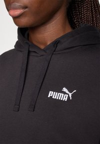 Fekete kapucnis pulóver texturált anyagból, bal mellrészen fehér hímzett Puma logóval és zsinóros kapucnival.
