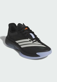 Scarpa sportiva nera con tomaia in rete, tre strisce grigie, accento arancione e suola in gomma testurizzata. Il sottopiede presenta un dettaglio blu traslucido.