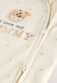 Kreemjas puuvillane ülikond heledate pruunide tähtedega. Kaunistatud kaelkirjaku tikandiga ja lukuga, mille küljed on valged. Tekstil on kiri "Ma armastan oma EMA".