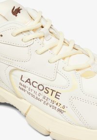 Lacoste sneakers in off-white leer met textuuraccenten, voorzien van crèmekleurige veters en bedrukte coördinaten op de zijkant.