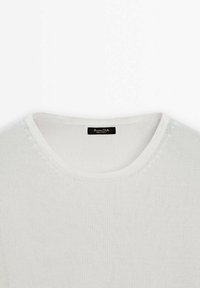 Pull léger en tricot blanc avec un col rond, des bords côtelés et une texture lisse. Comprend une étiquette de marque noire à l'intérieur du col.
