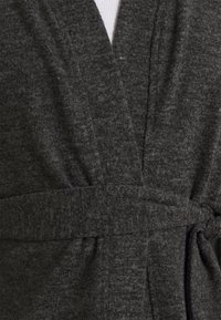 Kolsvarm grå omslagskofta med en mjuk, strukturerad stickning, som har ett bälte och en djup V-ringning.