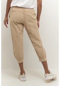 Beige cropped broek van lichtgewicht stof, met een elastische tailleband, omslagvoetjes en een relaxte pasvorm. Draagt met lichtgekleurde sneakers.
