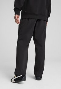 Melni sporta bikses ar brīvu piegriezumu un gludu, vieglu audumu. Iespējas ietver elastīgu jostu un sānu kabatas. Valkātas ar melnām kurpēm.