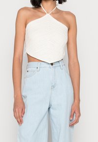 Bílý háčkovaný halter top s texturovaným diamantovým vzorem. V kombinaci se světle modrými džínami s vysokým pasem a širokými nohavicemi.