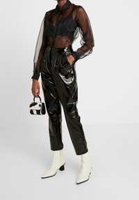 Průsvitná černá halenka s dlouhým rukávem a límečkem, kombinovaná s lesklými černými kalhotami s vysokým pasem a bílými špičatými kotníkovými botami. Součástí je malá kabelka.