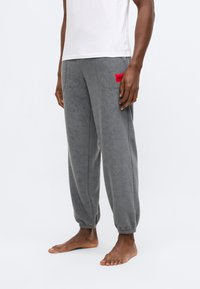 Γκρι παντελόνι φόρμας από φλις με ελαστικές μανσέτες και κόκκινο λογότυπο. Διαθέτει χαλαρή εφαρμογή και πλαϊνές τσέπες για λειτουργικότητα.