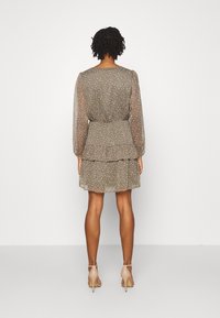 Robe brune transparente à motifs floraux, avec des manches longues et une jupe à volants. Associée à des chaussures à talons de couleur claire. Présente une taille cintrée.