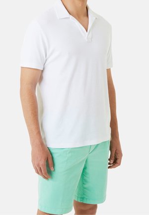 Mand iført kortærmet hvid polo og mintgrønne shorts, stående foran en ensartet lys baggrund.