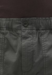 Γκρίζο παντελόνι με ελαστική μέση που διαθέτει στερεά υφή, κλείσιμο με κουμπί και ελαφριά πτυχές. Το ύφασμα έχει ελαφριά και ομαλή εμφάνιση.