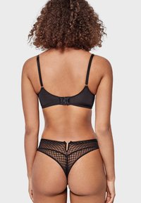 Black lingerie set featuring a smooth fabric bra with adjustable straps, and a sheer fishnet thong with geometric patterns and a cut-out detail.