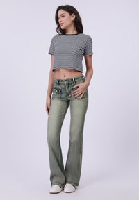 Zwart-wit gestreepte cropped t-shirt gecombineerd met lichtgroene, uitlopende jeans met zakken en een vervaagde textuur. Witte schoenen maken de outfit compleet.