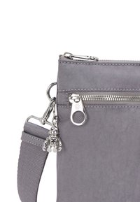 Borsa in tessuto grigio con chiusura a zip, minuteria argentata, una tasca esterna e un charm decorativo. Presenta una tracolla removibile.