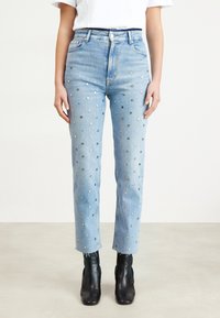 Ljust blå denimjeans med metalliska prickdekorationer, rak benpassform och fransade fållar. I kombination med svarta ankelstövlar.