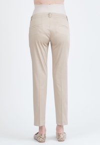 Un pantalon beige avec une taille ajustée, des jambes droites et deux poches arrière. Le tissu semble lisse et léger. Les chaussures sont en imprimé serpent.