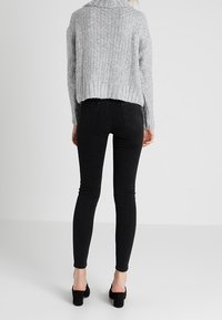 Grauer gestrickter, kürzerer Pullover mit hochgeschnittenem Kragen, kombiniert mit hochgeschnittenen schwarzen Skinny Jeans und schwarzen High-Heels.