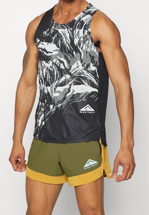 Man wearing black, white, and gray abstract patterned sleeveless top with olive green and yellow Nike Trail running shorts.