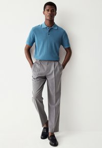 Blå ribbad pikétröja kombinerad med grå byxor med kritstrecksrand. Outfitten kompletteras med svarta loafers.