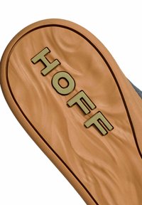 Suela de un zapato con textura de goma marrón claro; presenta texto dorado en relieve que dice "HOFF" y un diseño suave y ondulado.