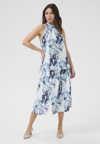 Hals jurk met bloemenpatroon en gelaagd ontwerp in blauw-, wit- en navytonen; lichte stof met een vloeiende rok; afgewerkt met neutrale hakken.