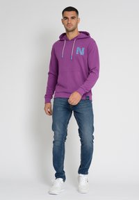 Violetti huppari, jossa sininen kuvioitu "N" logo, etutasku ja kiristysnauha hupussa. Yhdistetty sinisiin farkkuihin ja valkoisiin lenkkikengiin.