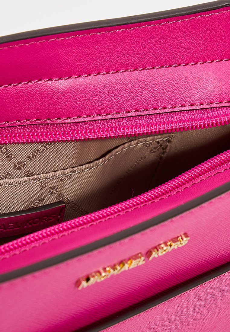 Interieur van een roze leren handtas met een gladde textuur, een ritszak en een merklabel. Voorzien van gouden hardware en een subtiel voeringpatroon.