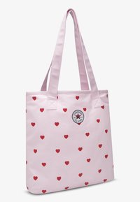 Φωτεινή ροζ τσάντα ώμου με κόκκινο μοτίβο καρδιάς, ορθογώνιο σχήμα, διπλές ανθεκτικές λαβές και κυκλικό λογότυπο Converse All Star.
