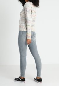 Mehrfarbiger, gestrickter Pullover mit Rundhalsausschnitt, kombiniert mit hellgrauen Skinny Jeans und schwarz-weißen Sneakern. Strukturiertes Strickdetail vorhanden.