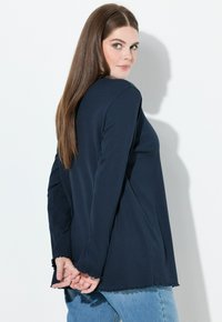 Maglietta a maniche lunghe blu navy con una finitura testurizzata, caratterizzata da una vestibilità morbida e un orlo leggermente sfrangiato. Abbinata a jeans azzurri.