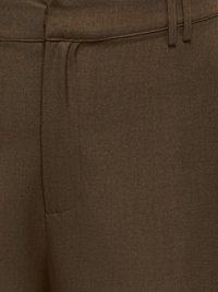 Gros plan d'un pantalon en tissu marron foncé montrant la taille, les passants de ceinture et les détails de la couture avant.