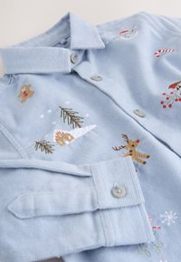 Light blue corduroy shirt featuring embroidered holiday motifs, including a gingerbread man, reindeer, trees, and snowflakes.
