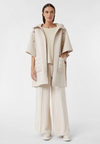 Cappotto in misto lana beige con cappuccio, due tasche trapuntate e zip frontale. Abbinato a un top beige testurizzato e pantaloni a gamba larga.