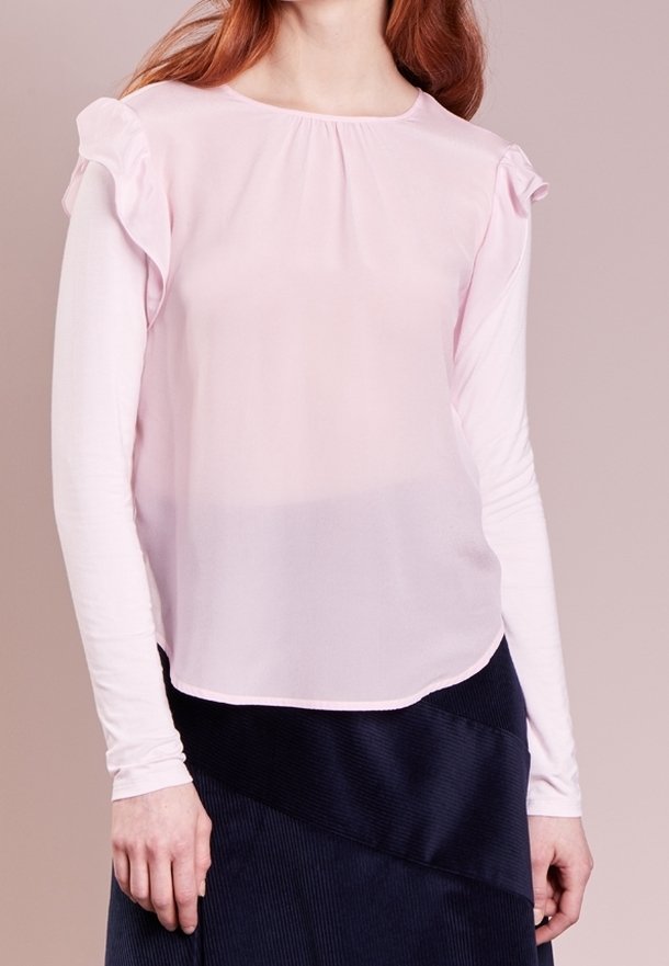 Blouse rose clair avec manches courtes à volants, encolure ronde et texture légèrement transparente, associée à une jupe en velours côtelé bleu marine.