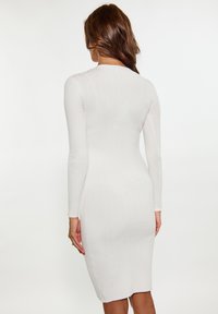 Långärmad, figurnära klänning i ribbat vitt trikåmaterial. Har rund halsringning och knä-lång fåll. Slät textur, enkel design.