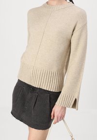 Beige stickad tröja med ribbad nederkant och trumpetärmar, matchad med en svart denimkjol med fransar i nederkant och veck.