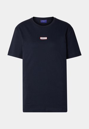 Granatowa bawełniana koszulka T-shirt z krótkimi rękawami i okrągłym dekoltem. Posiada prostokątną łatę z czerwono-białym logo na piersi.