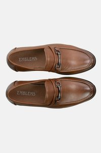 Los mocasines de cuero marrón presentan un acento metálico en tono plateado y detalles de costura. El interior tiene una textura con el logotipo de la marca.