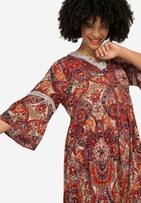 Vestido largo y fluido con estampado de paisley en rojo y naranja. Presenta un borde de encaje en el escote y mangas de campana. Tejido suave y ligero.