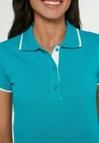 Teal polo shirt met een textuurstof, witte kraag en bies. Voorzien van drie knopen bij de hals en korte mouwen.