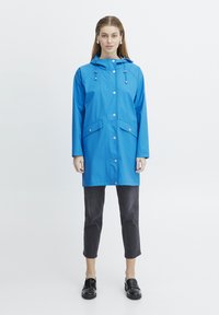 Blauwe waterdichte regenjas met een capuchon, drukknoopsluiting en twee voorzakken. Het ontwerp heeft lange mouwen en een comfortabele pasvorm.
