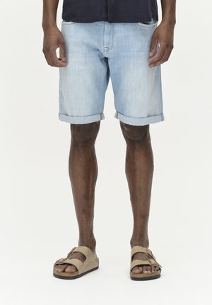 Lysblå denimshorts med oplagte opsmæk, der har fem lommer og diskrete stikninger, parret med brune sandaler.