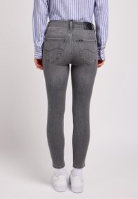 Los jeans skinny grises presentan una cintura alta, bolsillos traseros y una etiqueta de marca negra. Se llevan con una camiseta de rayas azul y blanca y zapatillas blancas.